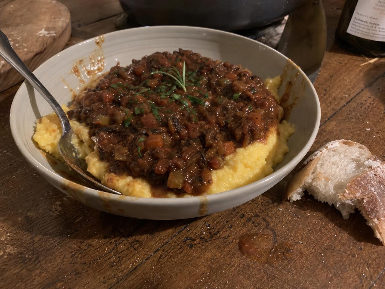 A bowl of mushroom ragu served over creamy polenta with a piece of bread on the side.