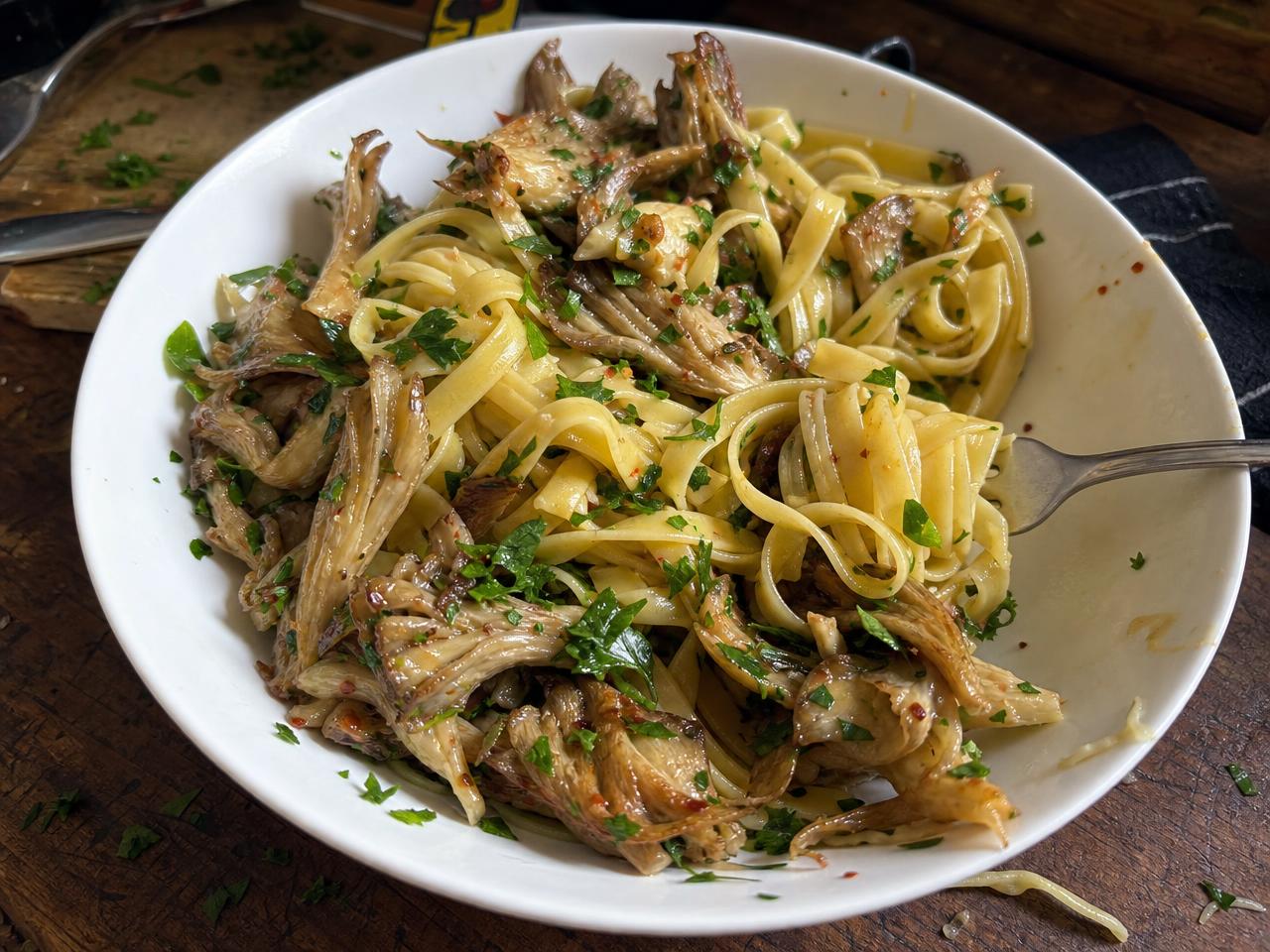 A bowl of pasta with seared mushrooms, garnished with parsley and chili flakes.