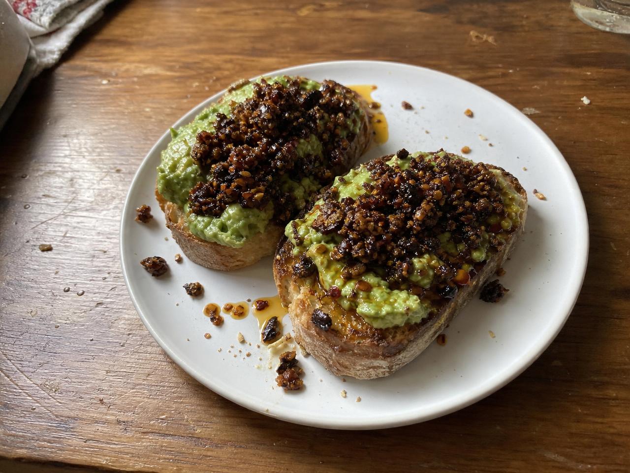 Two pieces of avocado toast topped with Mushroom XO Sauce on a white plate.