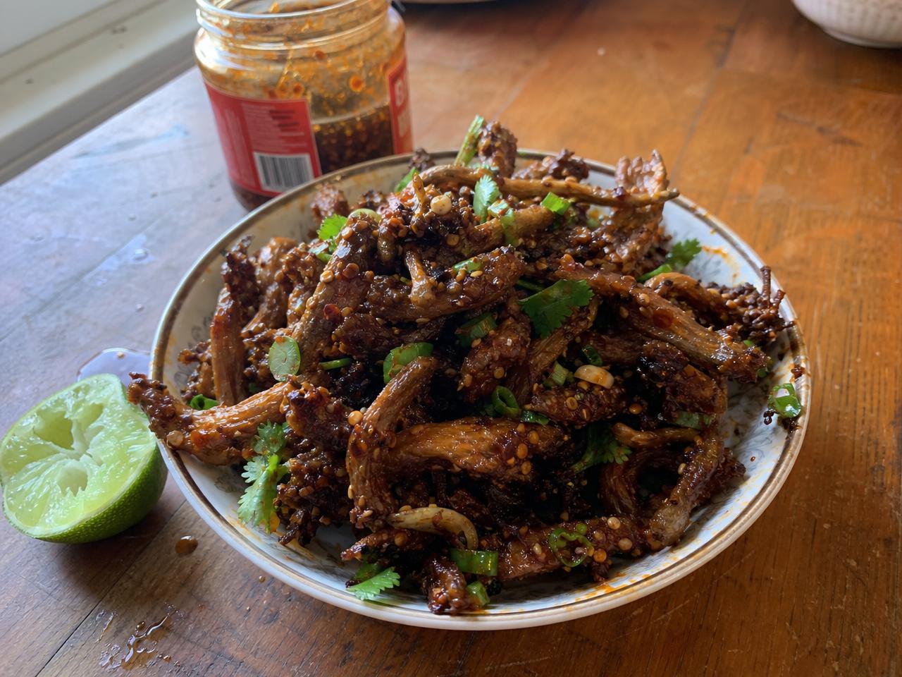 A plate of crispy fried oyster mushrooms tossed in chili crisp and lime, with a jar of chili crisp in the background.
