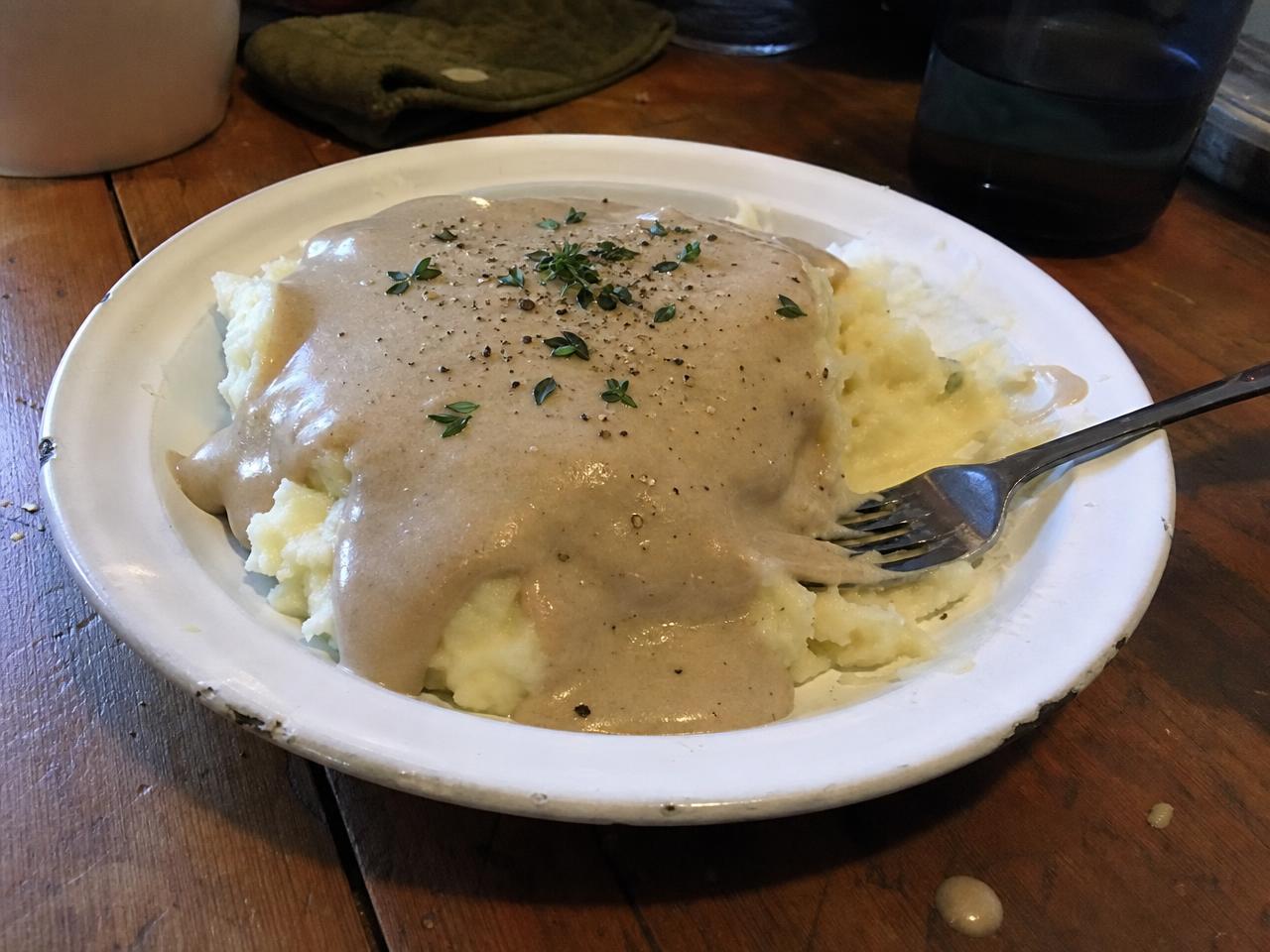 A plate of mashed potatoes topped with a creamy mushroom sauce and herbs.